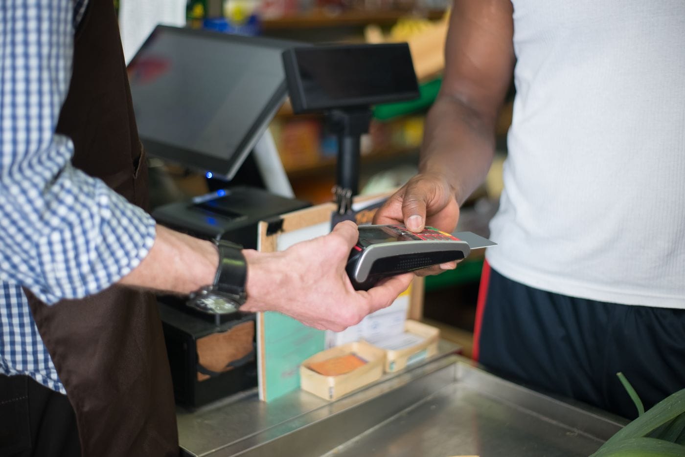 A customer taps a card on a payment terminal at a small shop checkout counter.